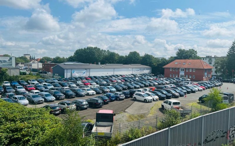 Blick von oben auf den voll belegten Außenparkplatz von Parkservice Bremen, dahinter die Halle des Betriebs