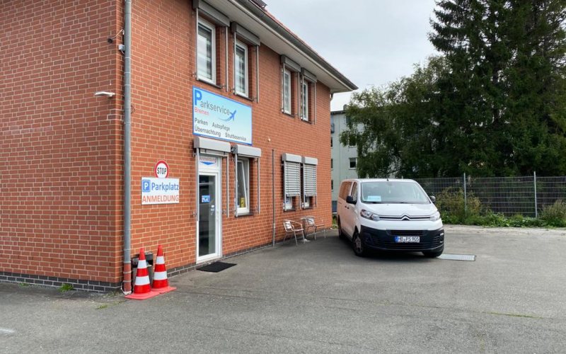 Anmeldung von Parkservice Bremen im Backsteingebäude, davor ein Fahrzeug des Shuttledienstes