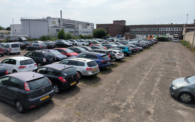 Reihen geparkter Fahrzeuge auf dem Gelände, im Hintergrund Hallen des Gewerbegebiets