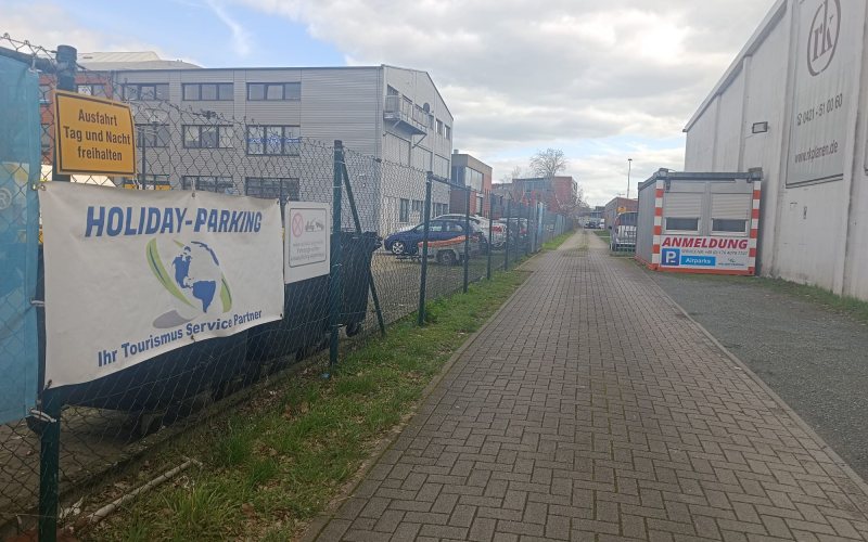 Einfahrt zum Gelände mit dem Banner „Holiday-Parking“ und dem Anmeldecontainer